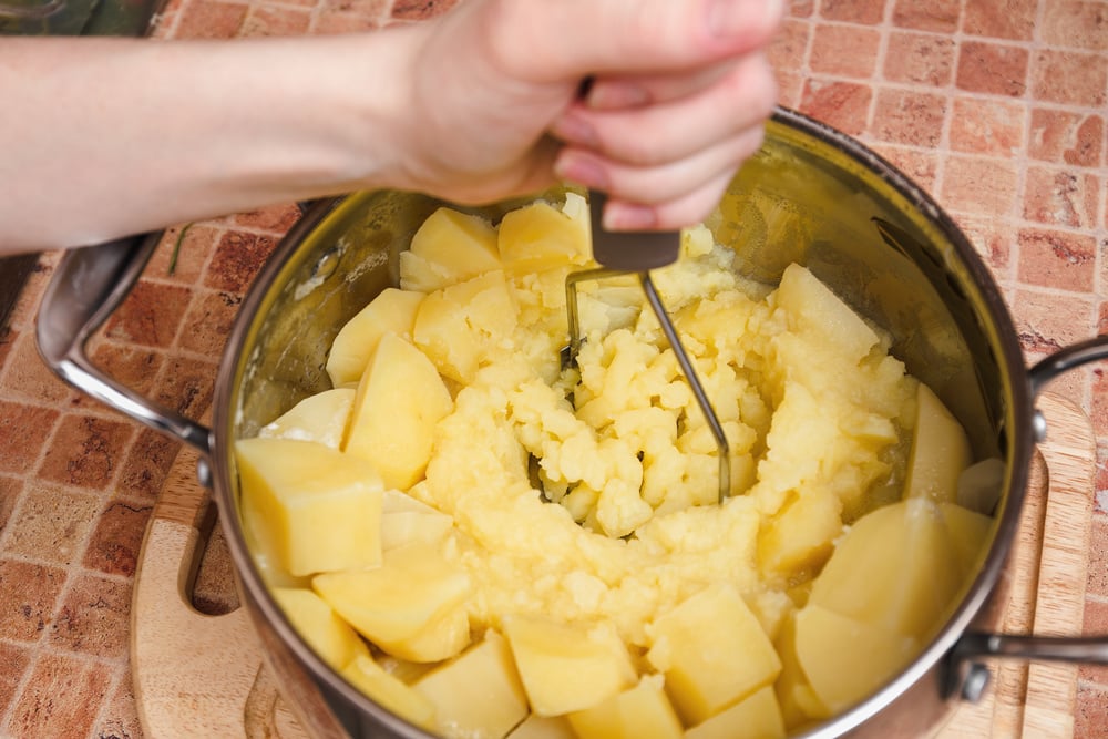 Woman preparing mashed potatoes with stainless potato masher. Cooking process, of mashed potato.